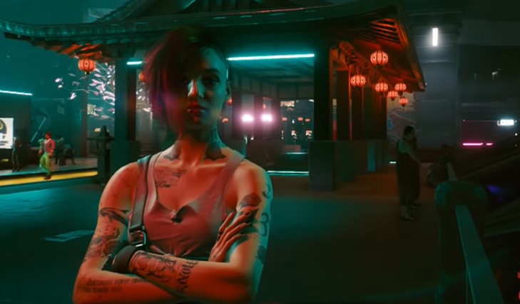 A screenshot of Judy Alveraz standing with arms crossed at night in Night City